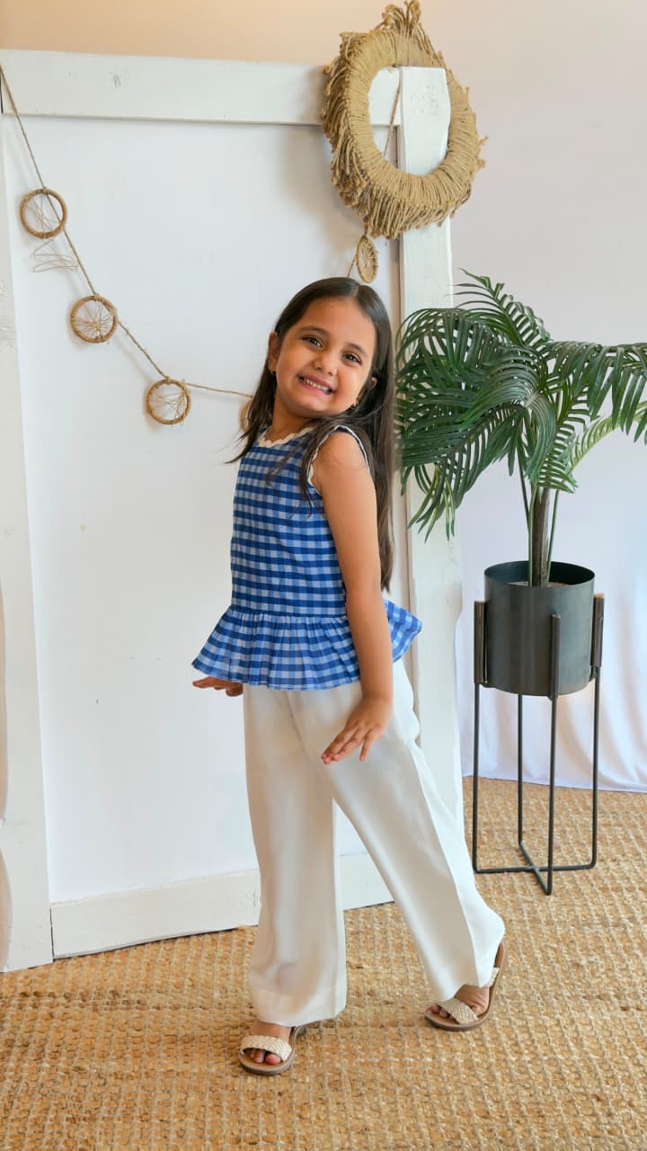 Back view of a girl wearing a blue gingham peplum top and white palazzo pants
