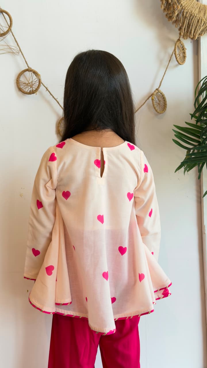 Girl wearing a blush heart-print flared top with matching pink pants