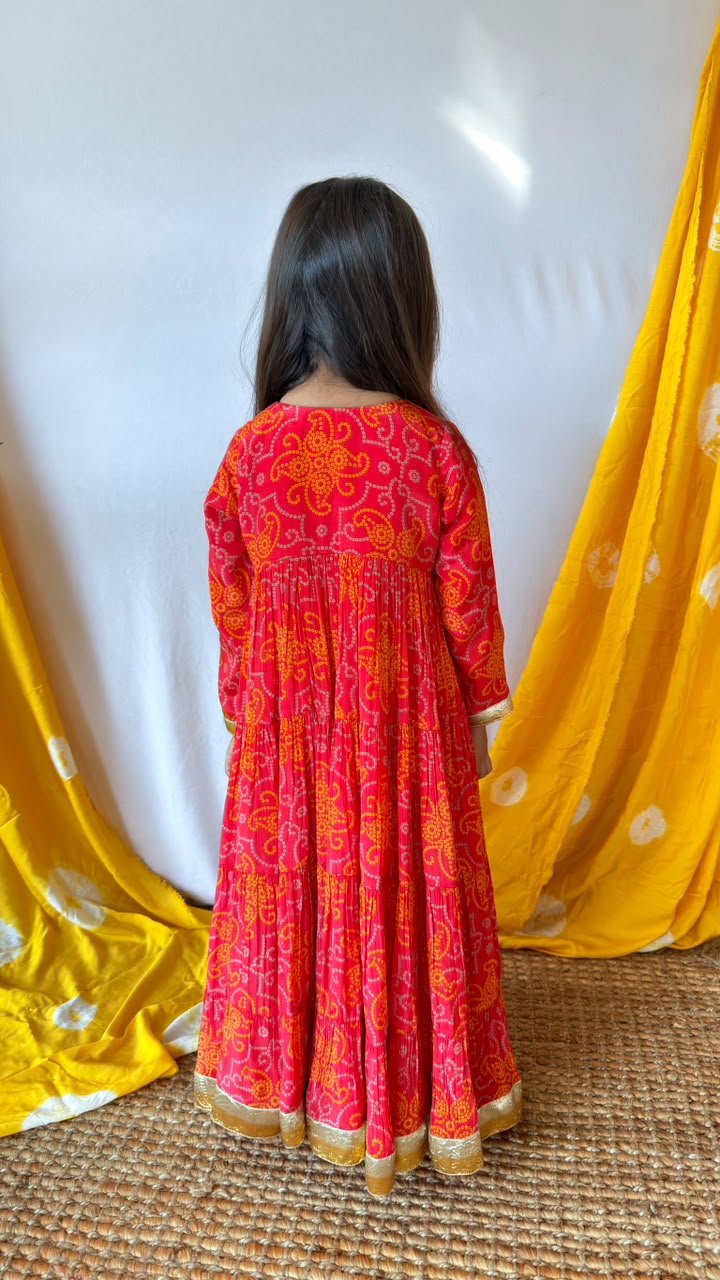 Front view of a girl wearing a red printed long-sleeve Anarkali dress with gold-toned trim