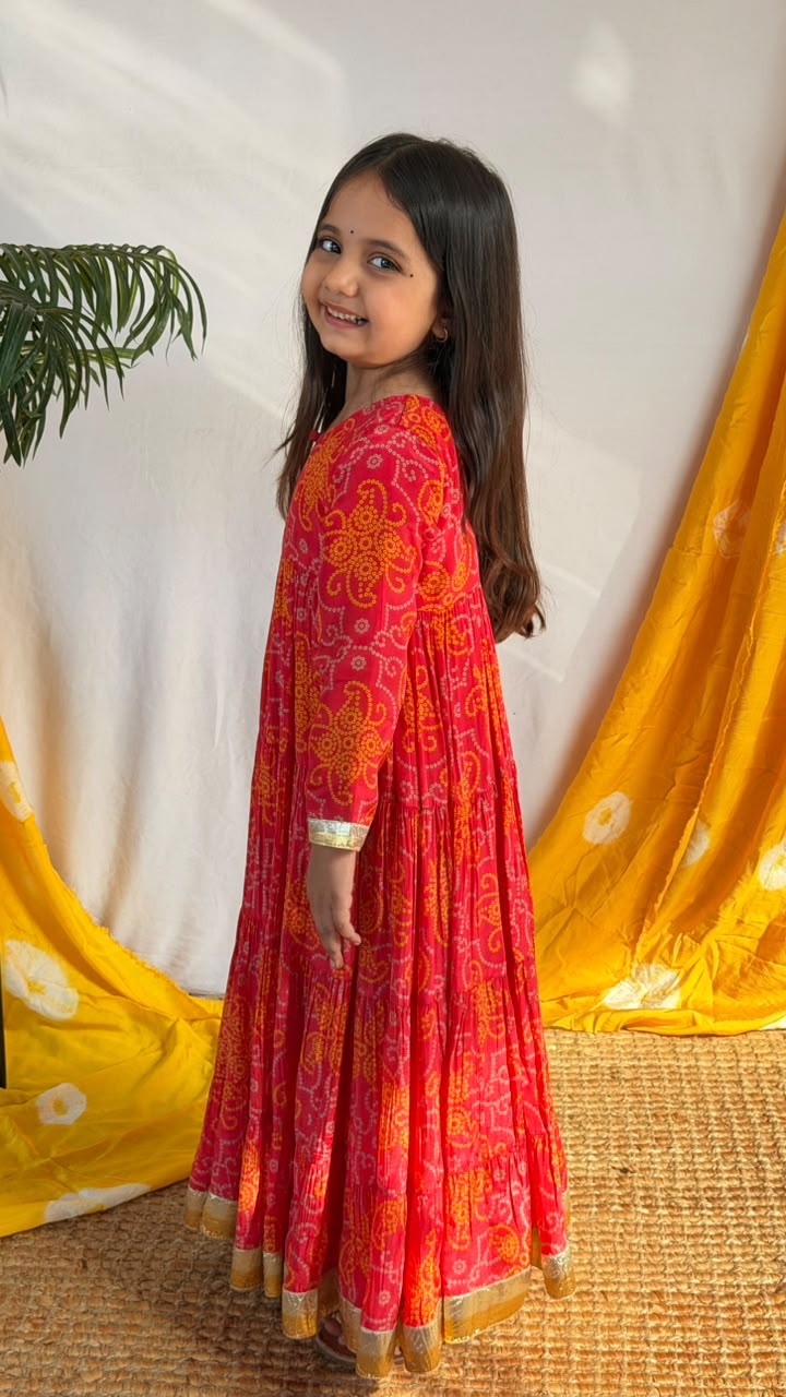 Side view of a girl wearing the red printed Anarkali dress with gold-toned cuff and hem trim